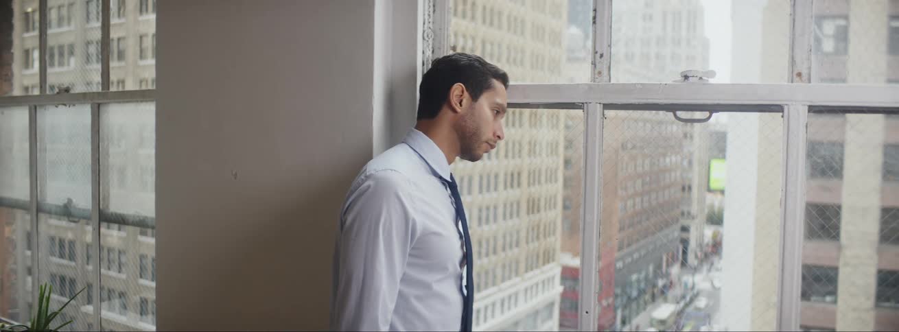 Businessman with tie and shirt looks out the office window at city streets