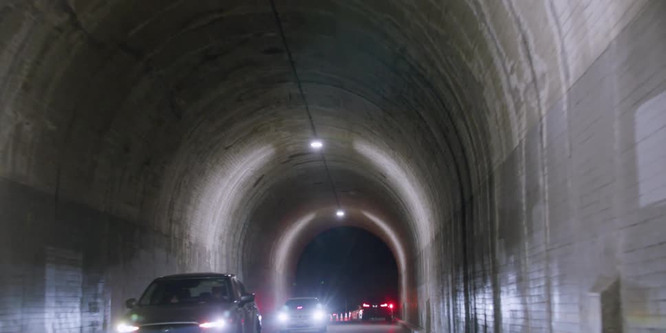Cars and people are moving through a tunnel at night