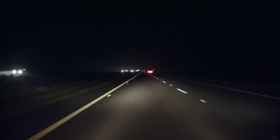 Automobiles travel on a road at night and the reflectors on the road shine from the headlights