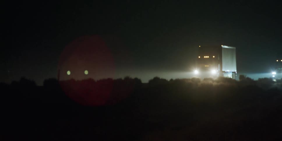 The bright headlights on trucks and cars shine as they travel on a freeway at night