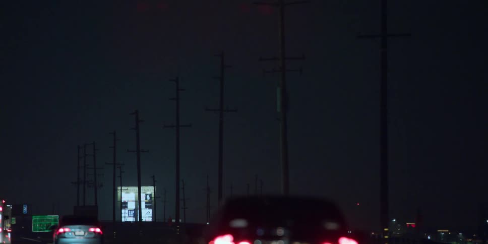 Automobiles travel at night on a road lined with utility poles