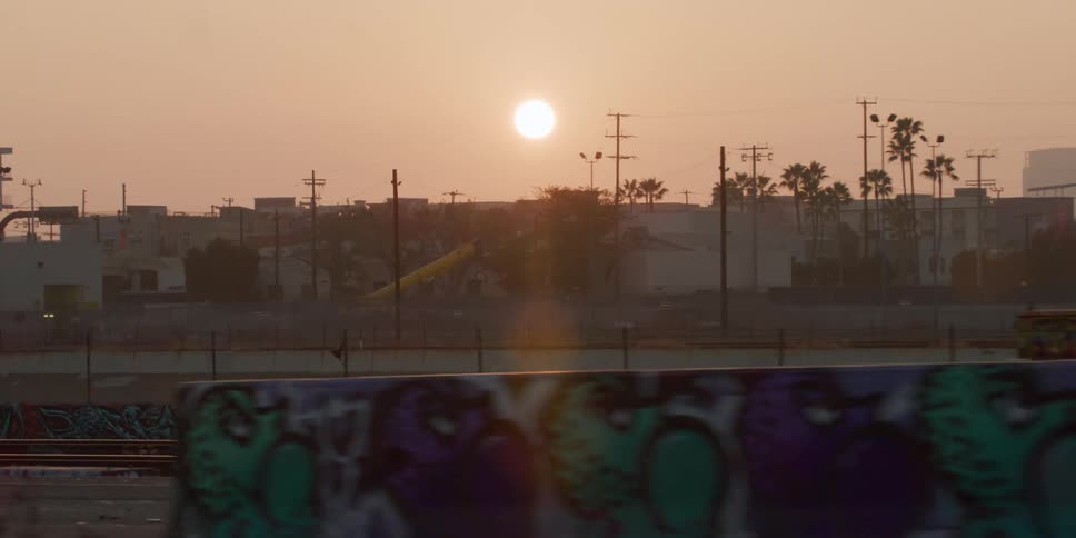 The sun rises over buildings with spray painted concrete barriers along the roadside