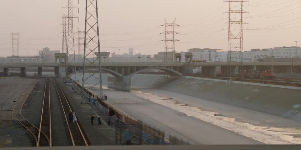 A truck travels over a bridge surrounded by utility towers and rail road tracks nearby