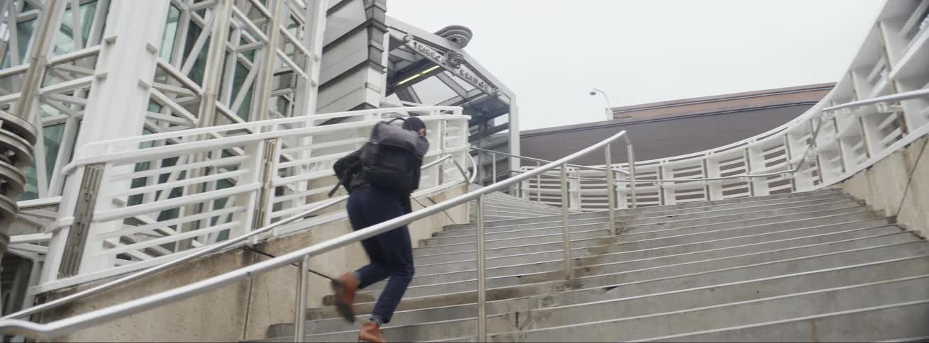 Man with a backpack runs up a flight of stairs at a stadium