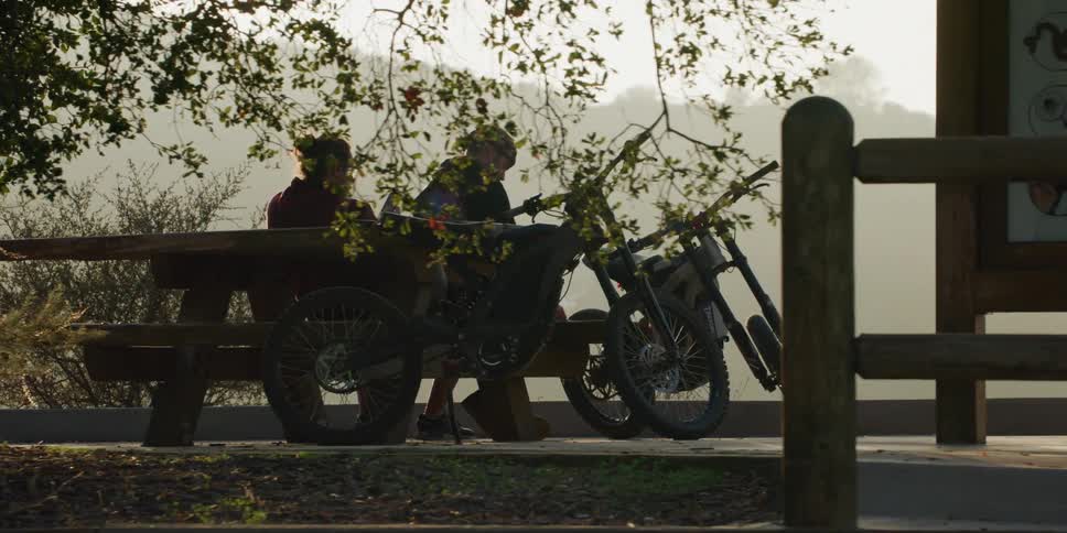 Two men sitting on a bench near a cliff with a nature view with their bicycles parked next to them