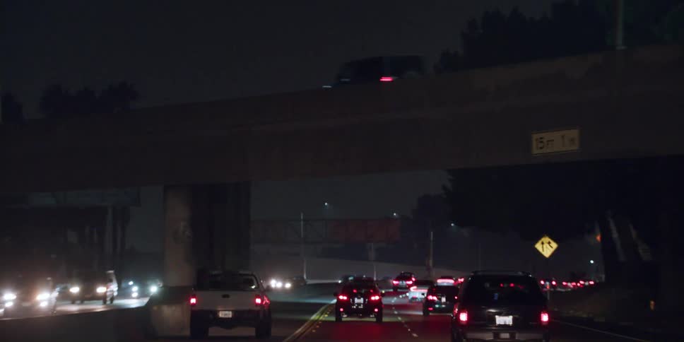 Automobiles are traveling on a freeway at night and under an overpass as other vehicles travel across the bridge above