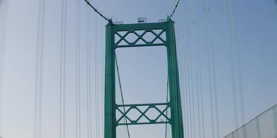 Vehicle crosses suspension bridge with turquoise tower