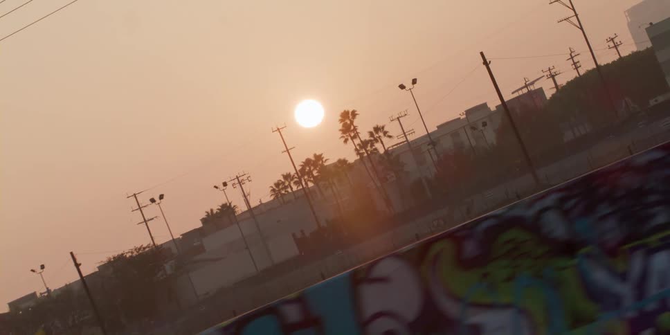 Sun grows in a red sky over buildings and graffiti road barriers