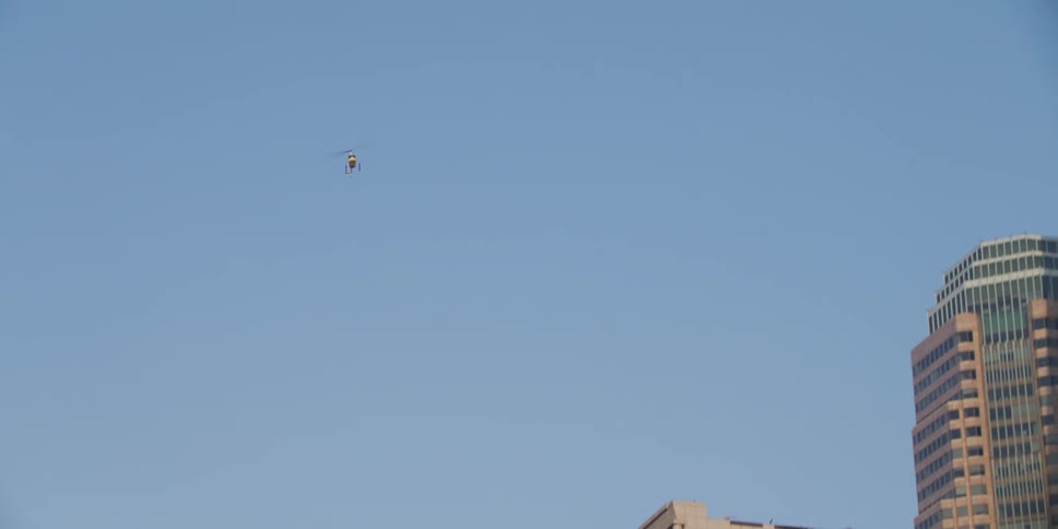 A helicopter flies above the tall city buildings