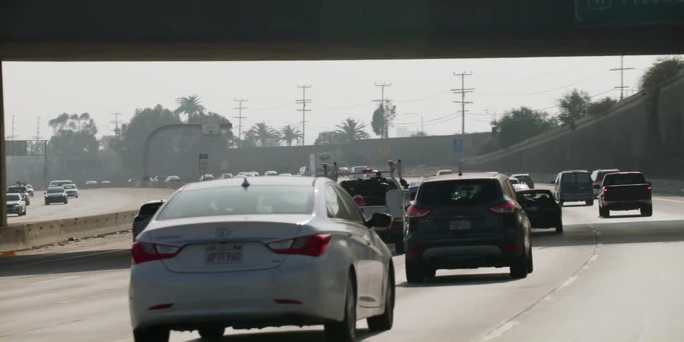Automobiles are traveling on a highway and through an overpass and utility towers are in the distance
