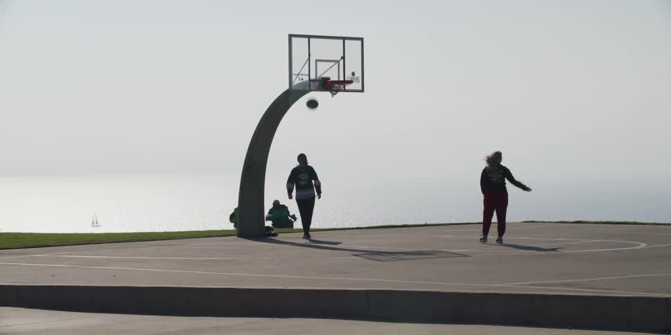 Two people shooting hoops on a court at the beach on a breezy day