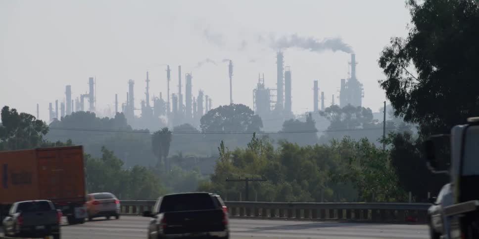 Vehicles travel on a highway as a factory sits in the distance