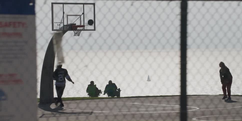 Two women throw layups on a basketball court along the coast