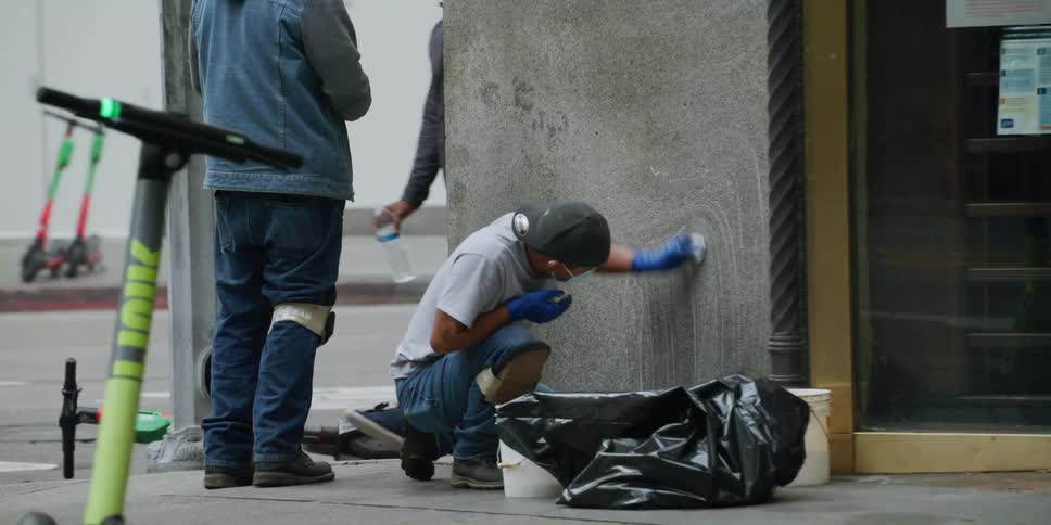 Person stands near worker cleaning wall as a pedestrian walks by