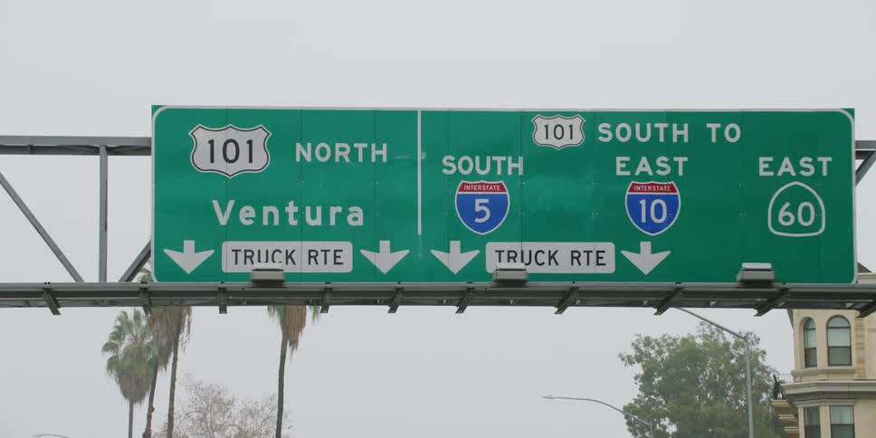 Large green rectangular sign over a highway indicating directions