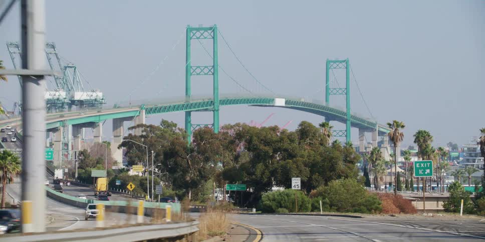 Traveling along the highway approaching a very tall suspension bridge over a port and harbor area in the daytime