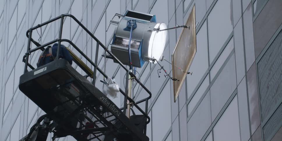 A cherry picker holds a spotlight and person by the building