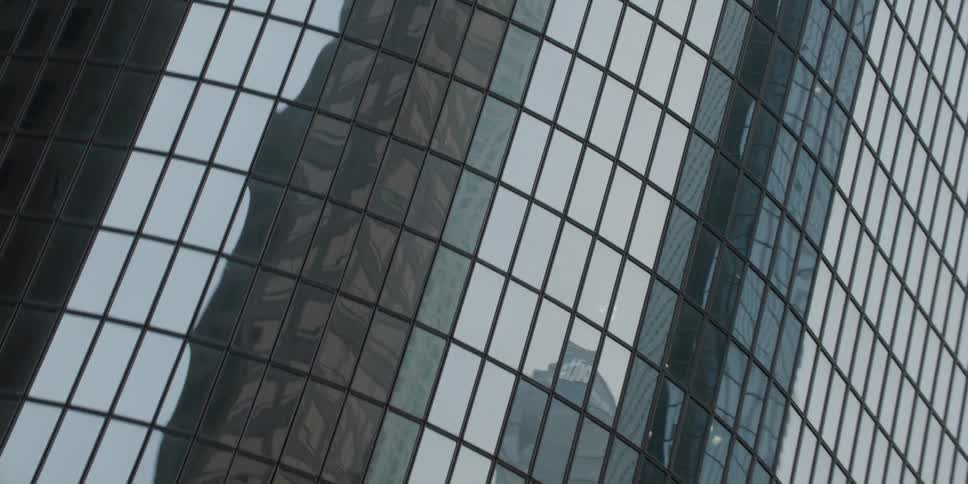 The mirror finish on the windows of a tall skyscraper reflect the sky and other buildings