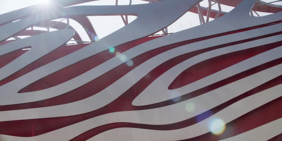 Sun shines down onto building with creative abstract wave details against a red background