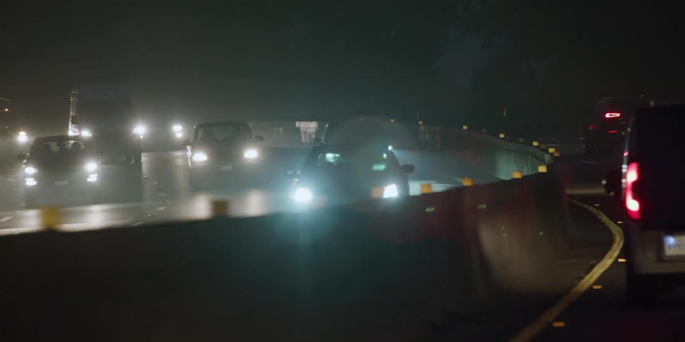 Headlights and tail lights shine brightly in the darkness as traffic on a busy highway moves around a bend