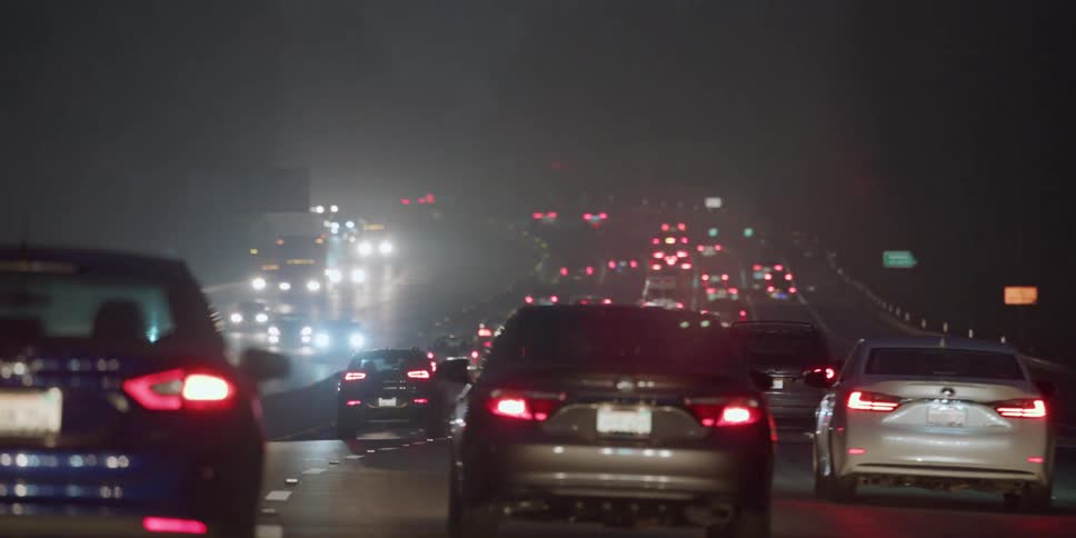 Cars and trucks travel on a highway at night in busy traffic