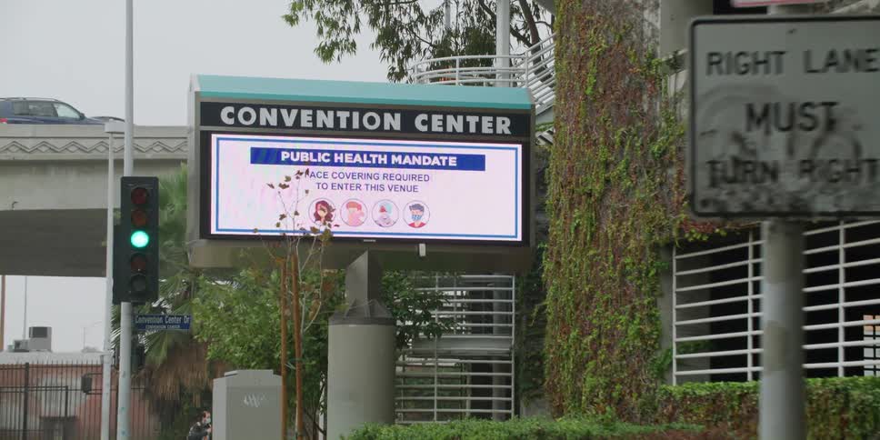 Pedestrian crosses street toward convention center with electronic sign