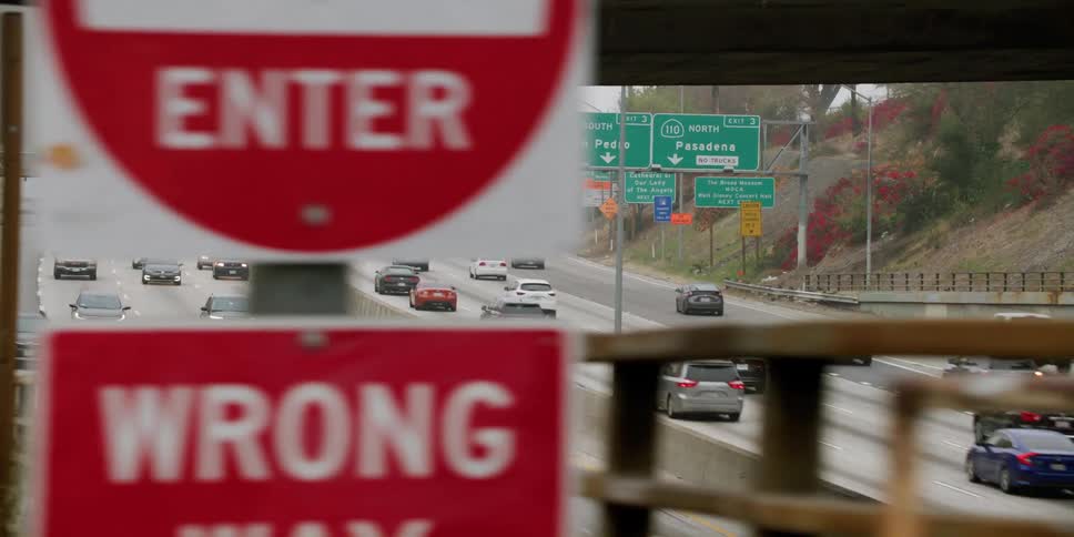 Automobiles travel on a freeway and go under a bridge and other vehicles are getting on the bridge