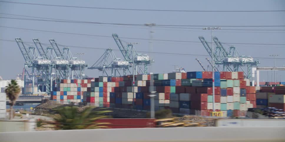 Traffic moves along controlled access highway passing stacked shipping containers and loading cranes