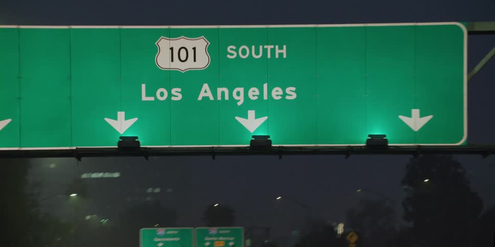 Directional signs hang over the traffic on a highway at night