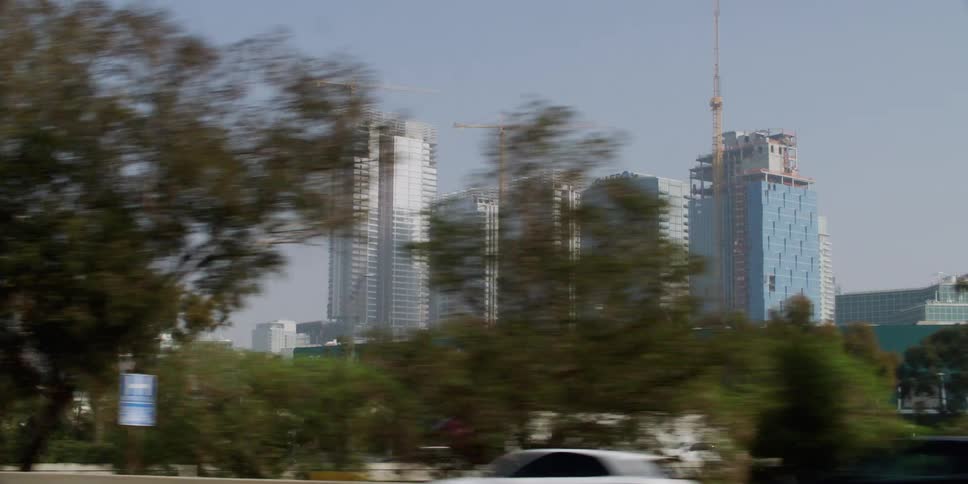 Distant view of cranes and buildings seen from moving car on city highway