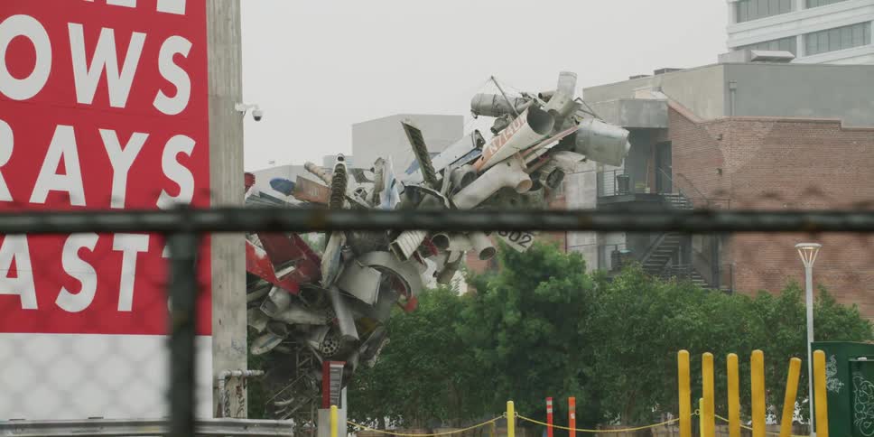 Sculpture made of junk sits between billboard and buildings