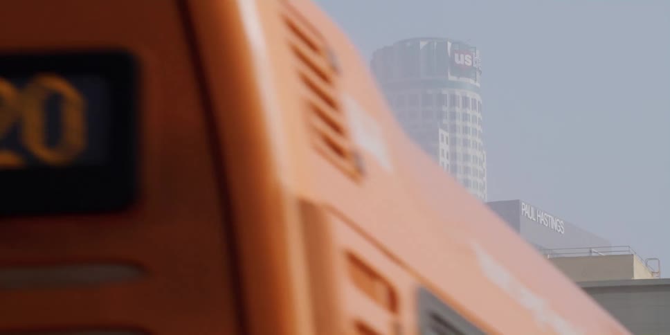 City bus travels past the city buildings and palm trees