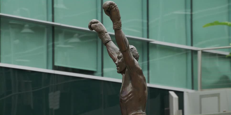 A statue of a man with his hands above his head cheering in a building