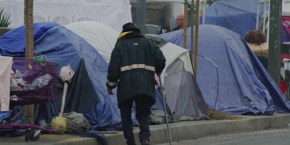 Man with a cane looks inside a tent in a homeless area of the city