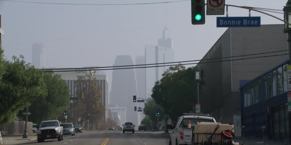 Trucks and cars travel toward a city skyline that looks grayed out by fog and haze
