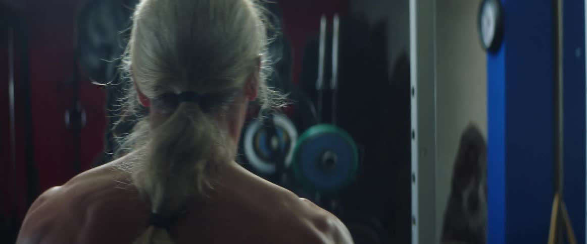 Muscular man with long ponytail walks in gym