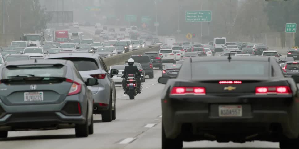 A motorcycle travels among the automobiles on a busy freeway on a foggy day