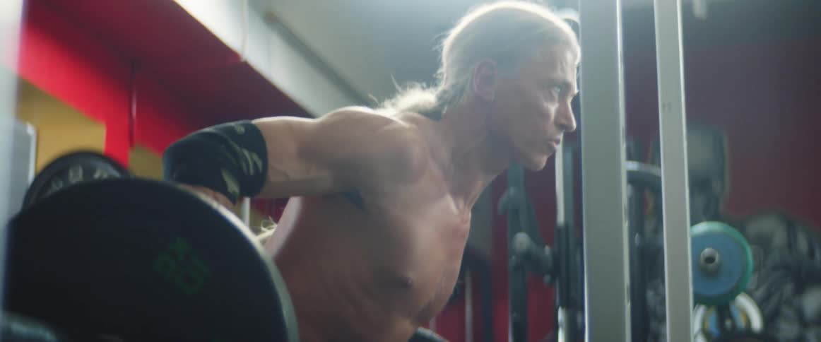 Man with a ponytail lifts a dumbbell in a gym