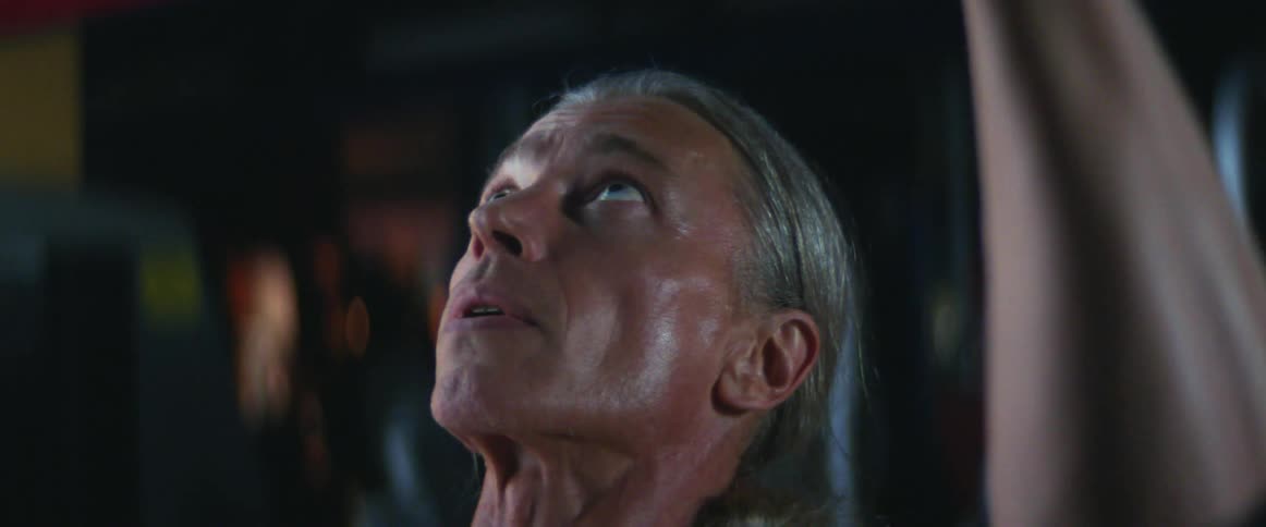 Middle aged and blue eyed man with gray ponytail works out in the gym