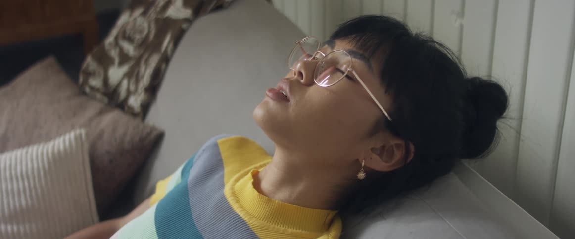Girl with glasses and stripped tshirt sitting on bed using smartphone in bedroom