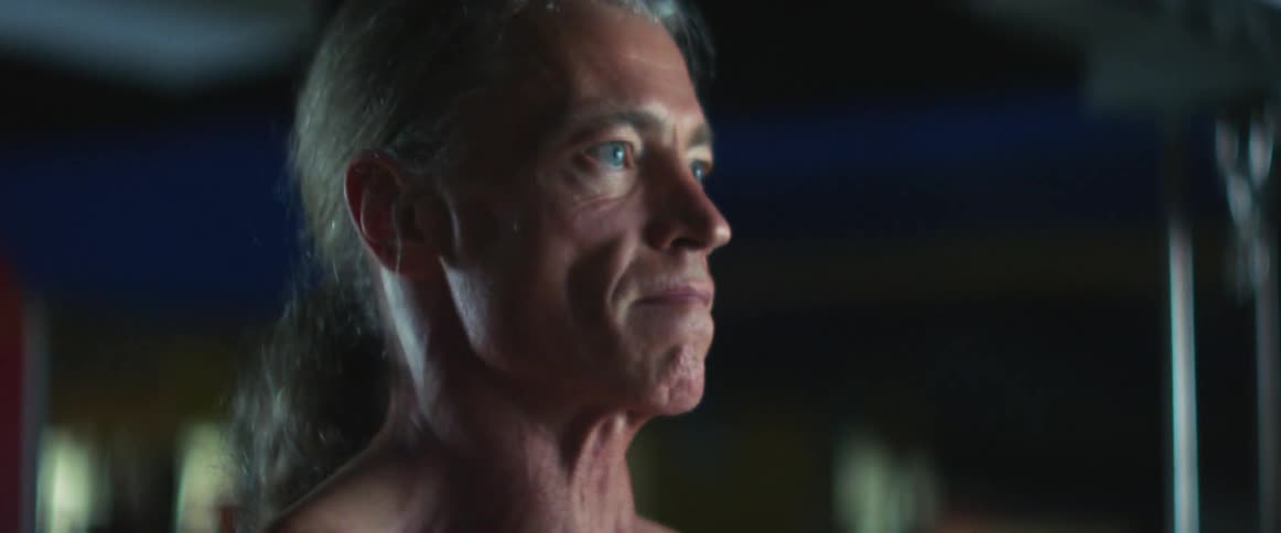 Middle aged and blue eyed man with long gray hair works out in gym