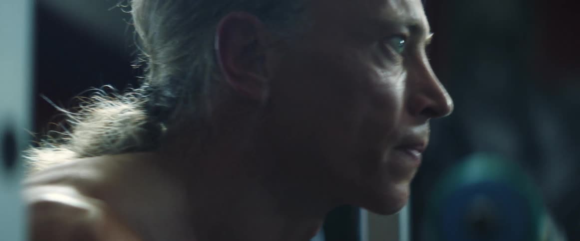 Middle aged and blue eyed man with gray ponytail gets ready to lift weight in gym