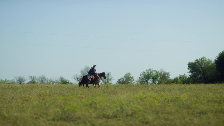 Men wearing hats shirts and vests ride brown and dark horses on grass in the field