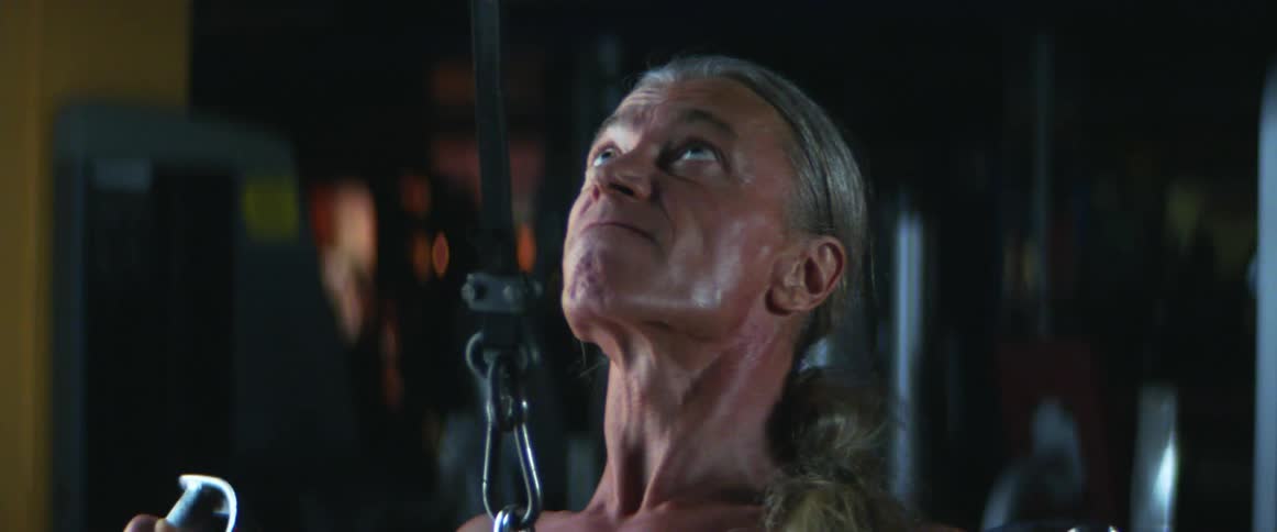 Middle aged and blue eyed man with gray ponytail works out in the gym