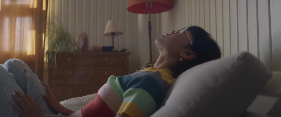 A teenage girl sits on a couch at home and texts and then sets her phone down and puts her head back on a pillow