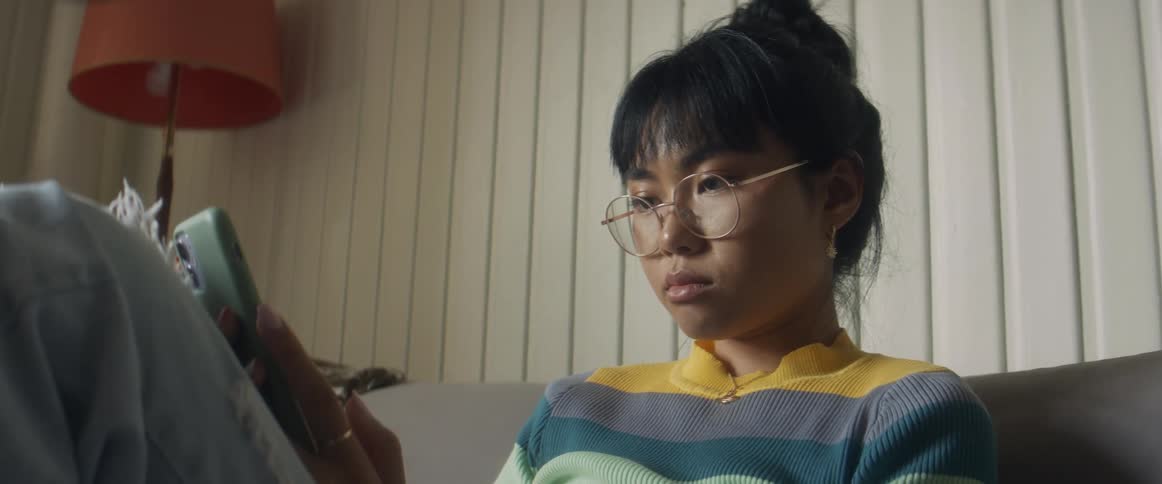 A teenage girl sits on a couch at home and looks at her cell phone