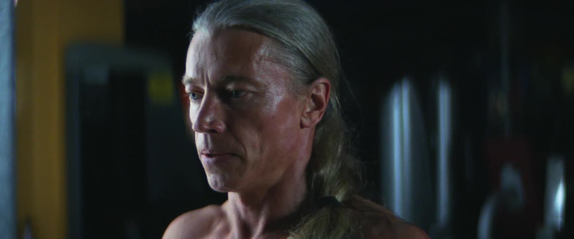 Middle aged and blue eyed man with gray ponytail breathes in gym