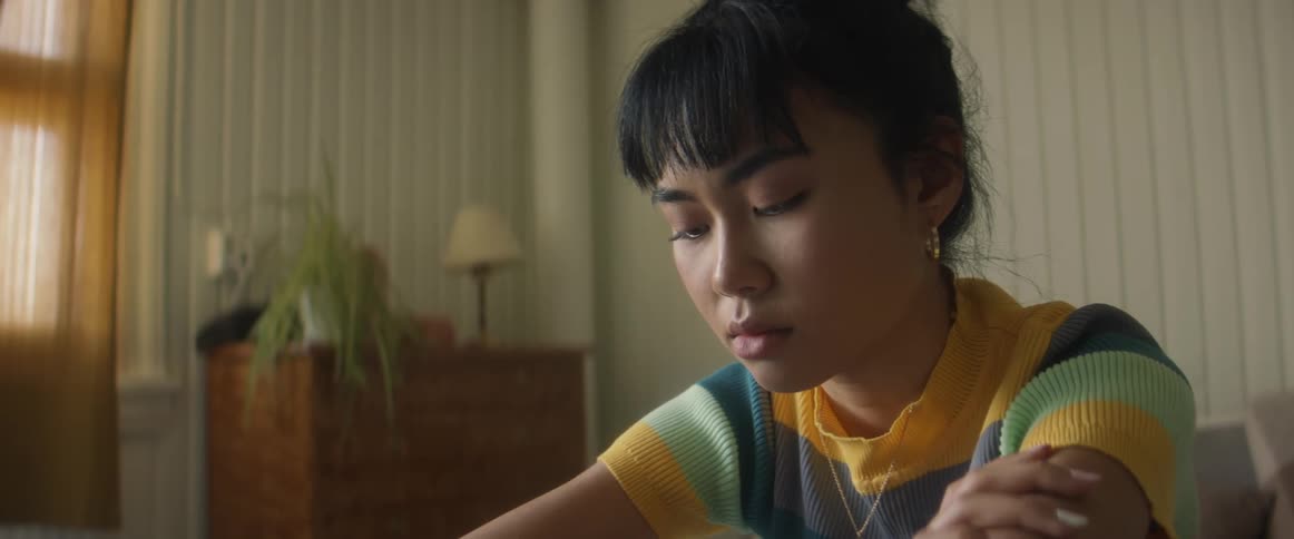Girl with stripped shirt earrings and necklace sits on bed in bedroom