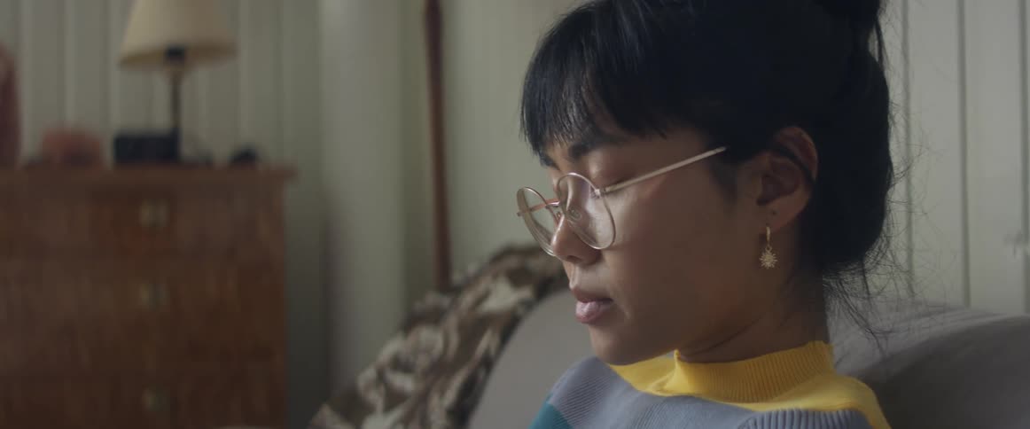 Asian woman wearing round eye glasses sits and is being thoughtful