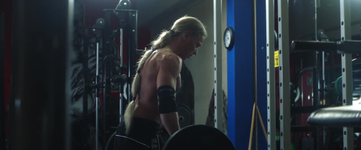 Middle aged muscular man with long gray ponytail works out in gym